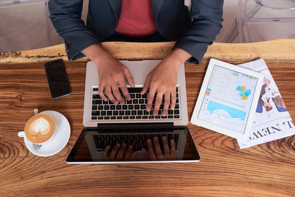 Hands of unrecognizable man sitting at wooden table in cafe and working on laptop