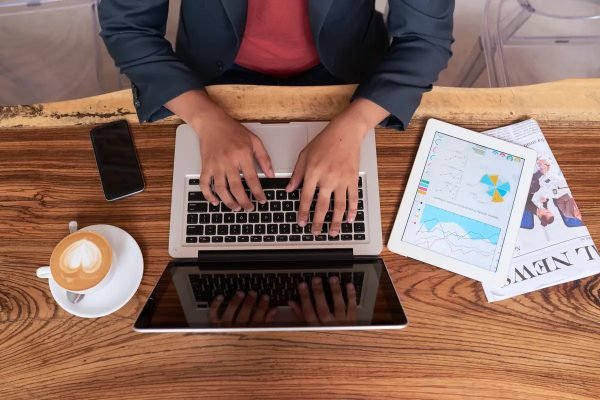 Hands of unrecognizable man sitting at wooden table in cafe and working on laptop