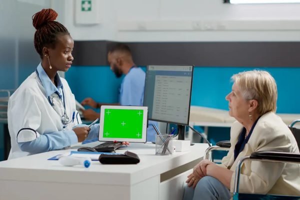 Physician holding tablet with horizontal greenscreen at appointment with woman in wheelchair. Using chroma key display with isolated copyspace and blank mockup background. Tripod shot.